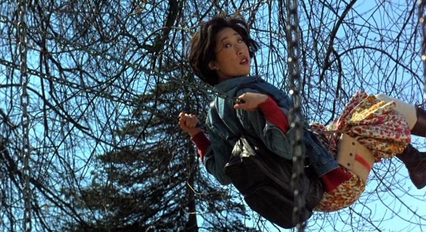 Double Happiness (1994) movie still: medium — A playground swing set positioned against a background of dense, leafless tree branches. A young woman…