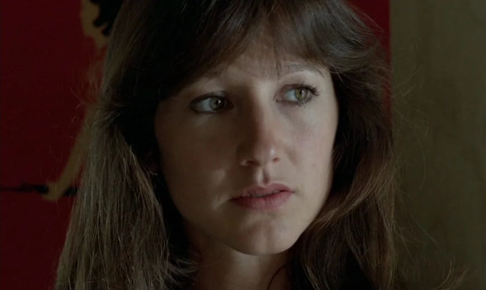 Every Man for Himself (1980) movie still: closeup — A close-up shot focuses on a young woman with long brunette hair. She stands in a dimly lit room…