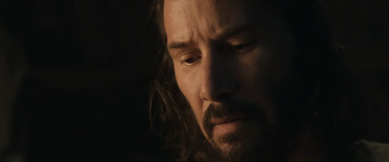 47 Ronin (2013) movie still: closeup — A dimly lit interior space with shadows obscuring the background. A middle-aged man with a full beard looks…
