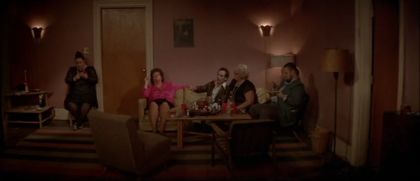 Blue Velvet (1986) movie still: wide — A dimly lit room with pink walls contains a sofa and several armchairs. Five people sit grouped together…