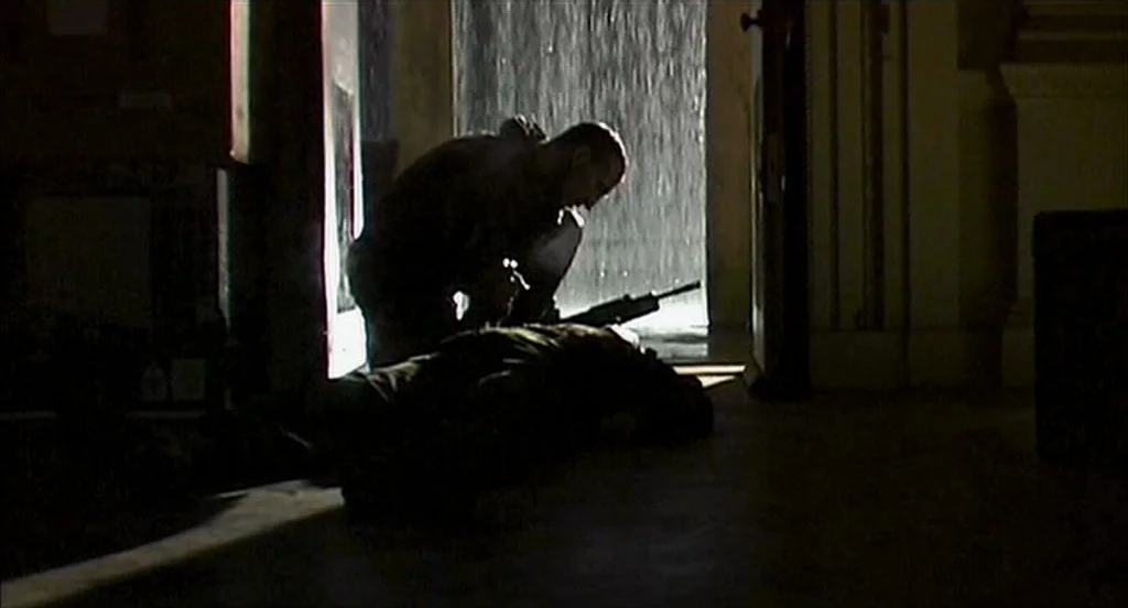 28 Days Later (2002) movie still: fullbody — A dark indoor threshold faces a brightly lit exterior during a heavy rainstorm. A man in tactical gear…