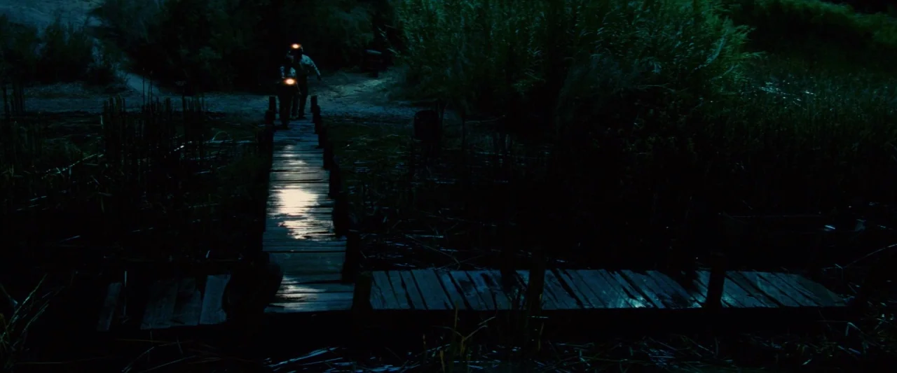 Piranha 3D (2010) movie still: wide — A wooden dock extends into dark water surrounded by dense, tall marsh grass. Two figures wearing headlamps…