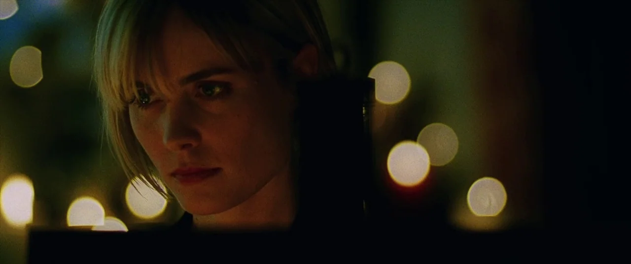Man on Fire (2004) movie still: closeup — A woman's face is illuminated in a dark setting with circular light flares in the background. She stares…