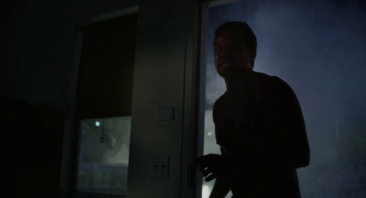 Velvet Buzzsaw (2019) movie still: medium — A dark interior room features a doorway leading out into a misty, nighttime environment. A shirtless man…