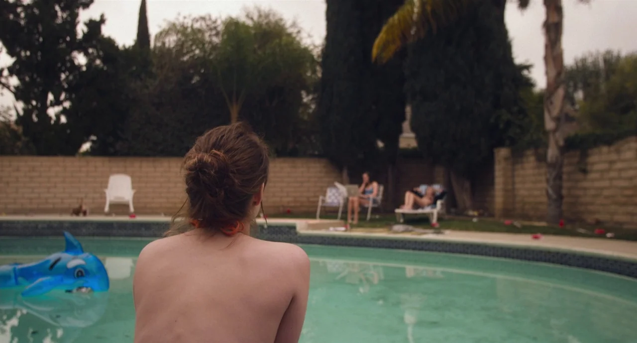Palo Alto (2013) movie still: medium — A residential backyard features an inground pool with a blue inflatable dolphin toy. Two other people lounge…