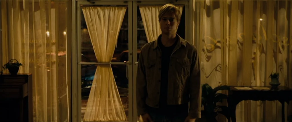 The Curious Case Of Benjamin Button (2008) movie still: medium — A dimly lit room features large glass doors draped with thin, golden curtains. A…
