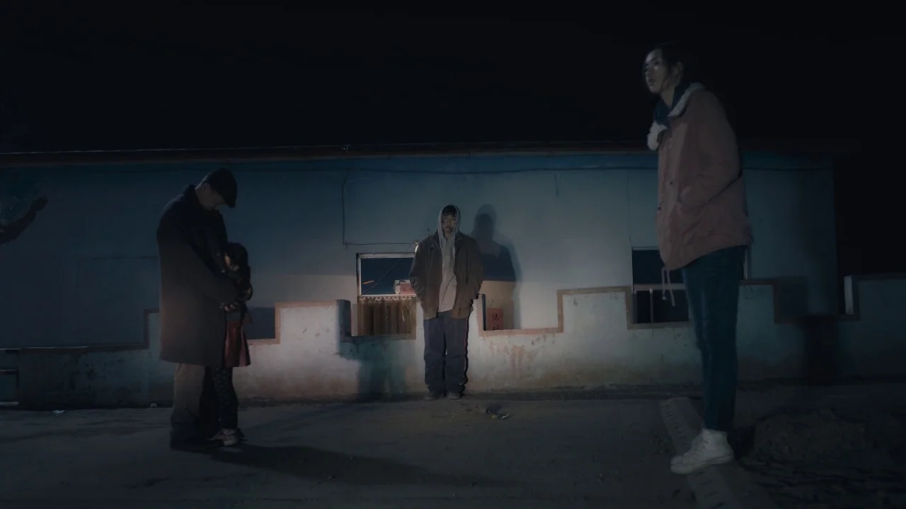 An Elephant Sitting Still (2018) movie still: wide — A dark outdoor space with a low concrete wall behind the figures at night. Three adults and one…