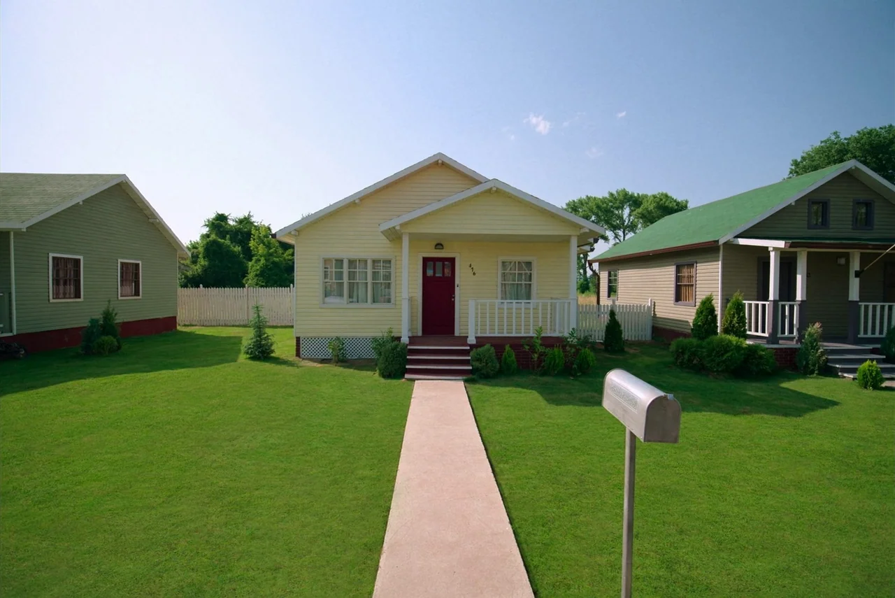 Barbarian (2022) movie still: wide — Three suburban houses stand on a sunny day with neatly manicured green lawns. A concrete walkway leads from the…