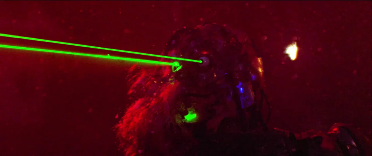 Christmas Bloody Christmas (2022) movie still: closeup — A dark red, atmospheric environment filled with suspended particles in the air. A humanoid…