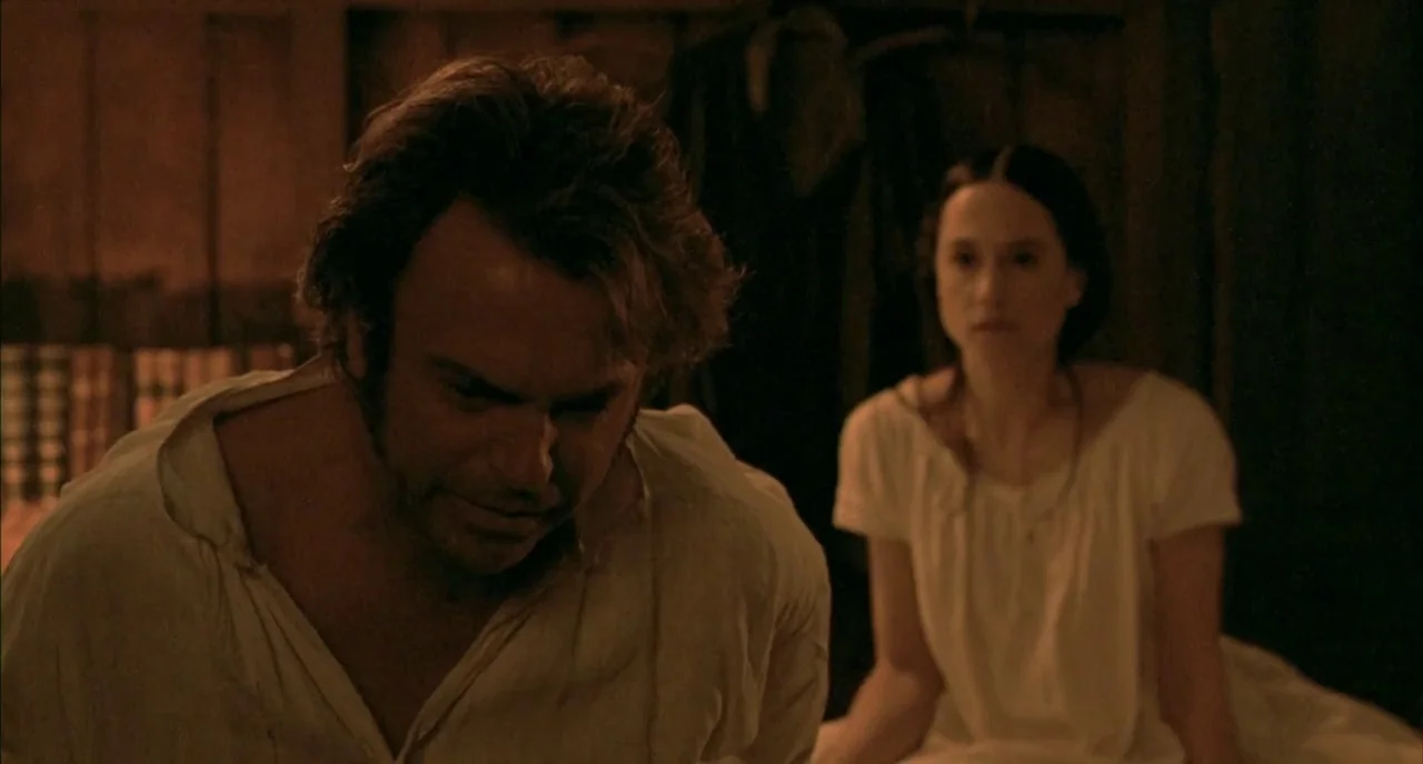 The Piano (1993) movie still: medium — A dimly lit room with rough wooden walls houses two figures. A man leans forward in the foreground while a…