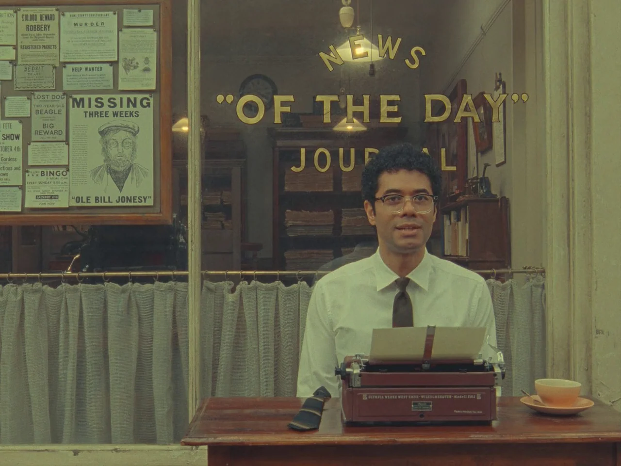 The Rat Catcher (2023) movie still: medium — A man sits behind a display window covered in various printed posters and text. He operates a vintage…