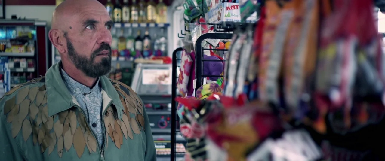 Here Comes The Devil (2012) movie still: medium — A man stands in the aisle of a small retail store with snack shelves. He is facing the shelves…