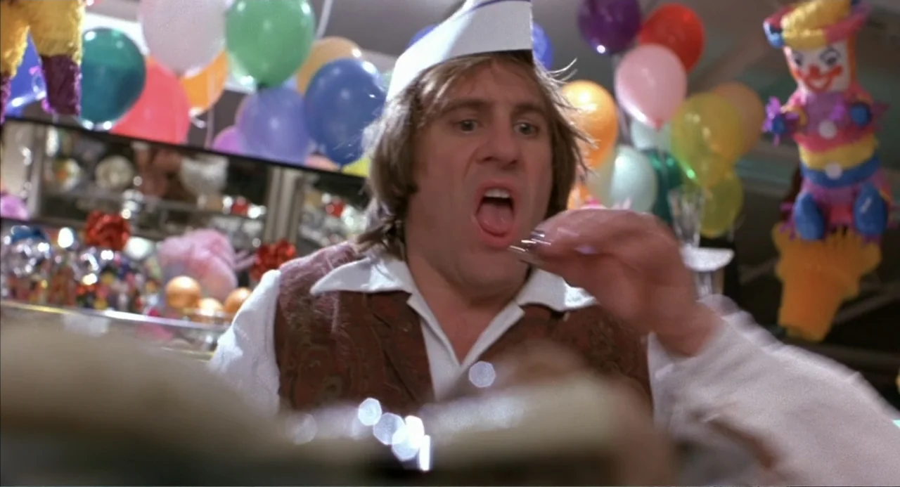 Bogus (1996) movie still: medium — A decorated interior space is filled with colorful balloons and a clown piñata. A man in a paper hat sits and…