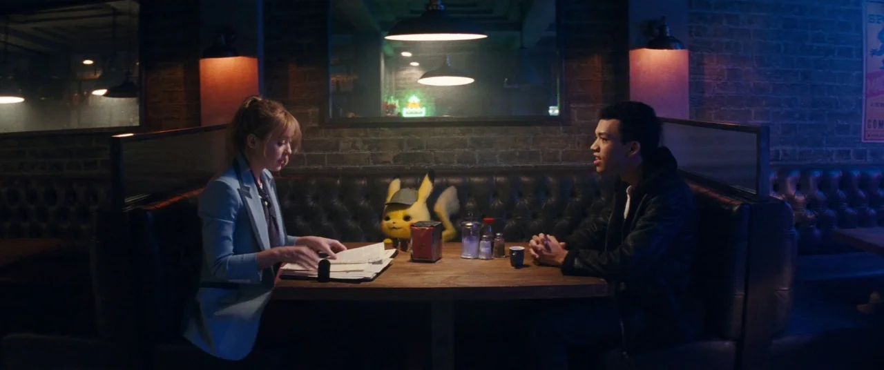 Pokémon Detective Pikachu movie still: medium — A dimly lit restaurant booth with a dark leather tufted bench against brick walls. Two people sit…