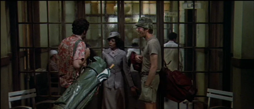 MASH (1970) movie still: medium — A hospital corridor features large glass-paned doors with a labeled laboratory sign visible. Three people stand in…