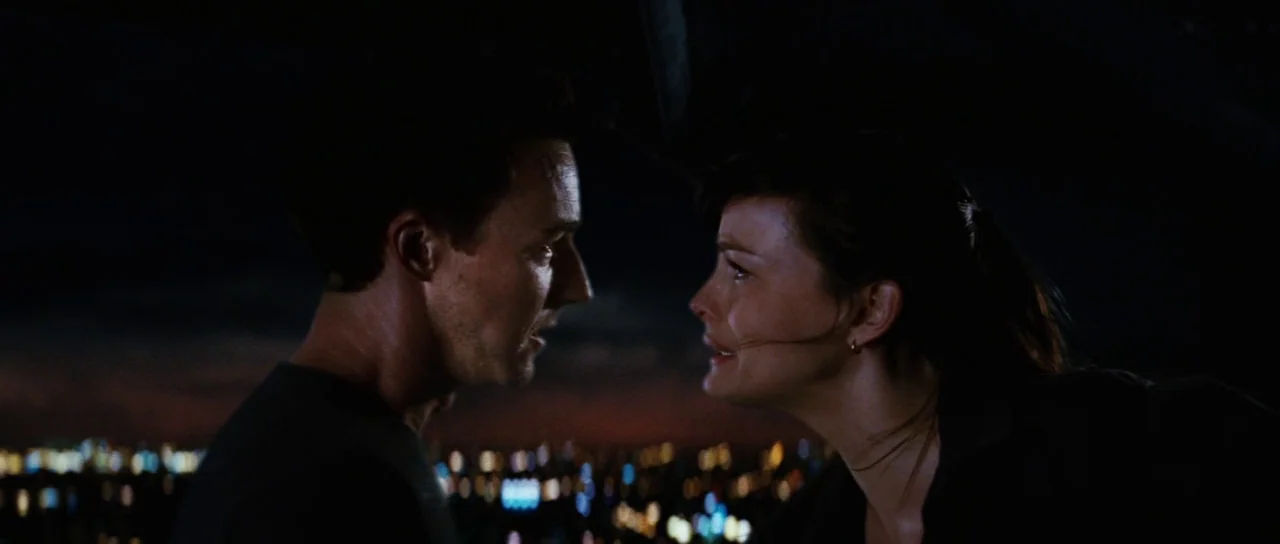 The Incredible Hulk (2008) movie still: medium — Two individuals stand closely on a dark rooftop overlooking a blurred distant cityscape. They are…