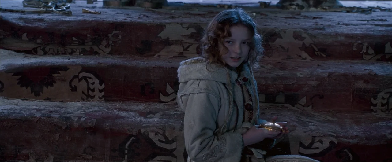 The Golden Compass (2007) movie still: medium — A dark, decaying interior staircase is covered in a worn and patterned carpet. A young girl sits…