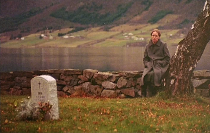 Autumn Sonata (1978) movie still: wide — A rural cemetery sits on the shore of a large lake with rolling green hills. A woman sits on a low stone…