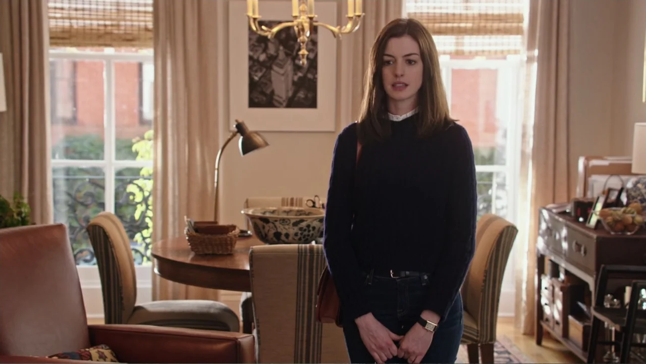 The Intern (2015) movie still: medium — A well-lit domestic living room featuring a wooden dining table and beige upholstered chairs. A woman with…