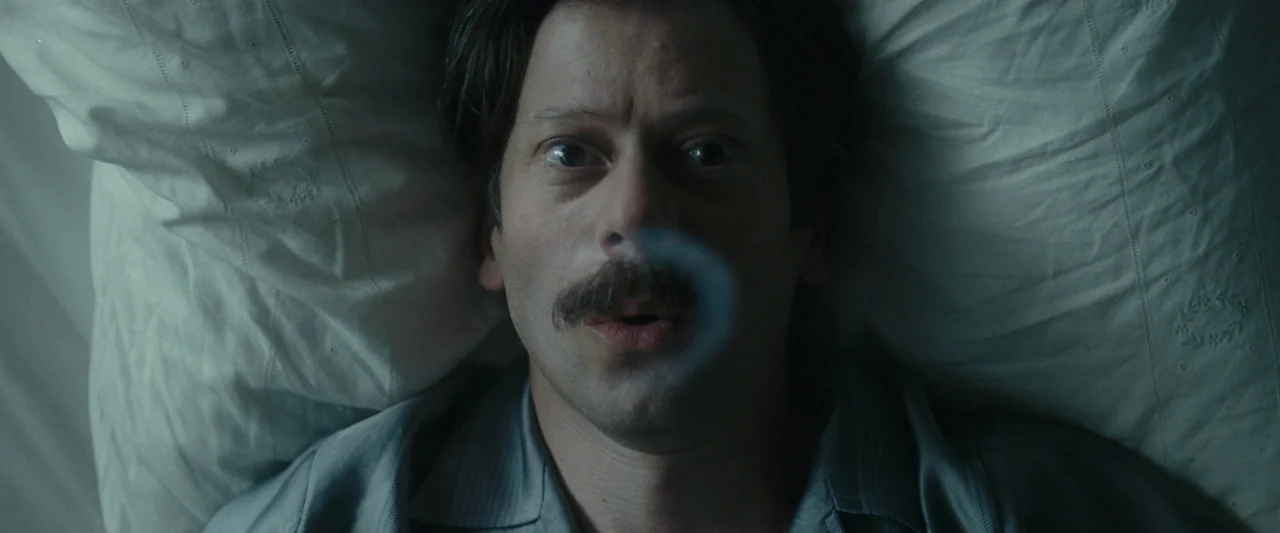 Chicken With Plums (2011) movie still: closeup — A man lies on a plain white pillow against a white sheet background. He stares upwards while…