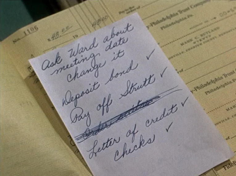 Marnie (1964) movie still: closeup — A handwritten task list rests on top of a vintage banking document. The paper is white with cursive ink writing…