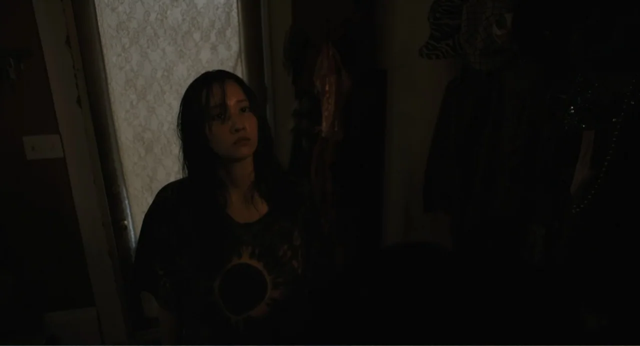 Mona Lisa and the Blood Moon (2022) movie still: medium — A dimly lit indoor hallway has a textured door curtain visible in the background. A young…