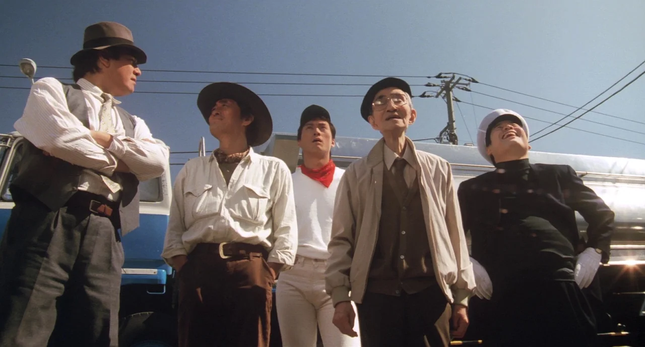 Tampopo (1985) movie still: fullbody — Five men stand in a line before a large parked tanker truck. They look toward the sky while sunlight…