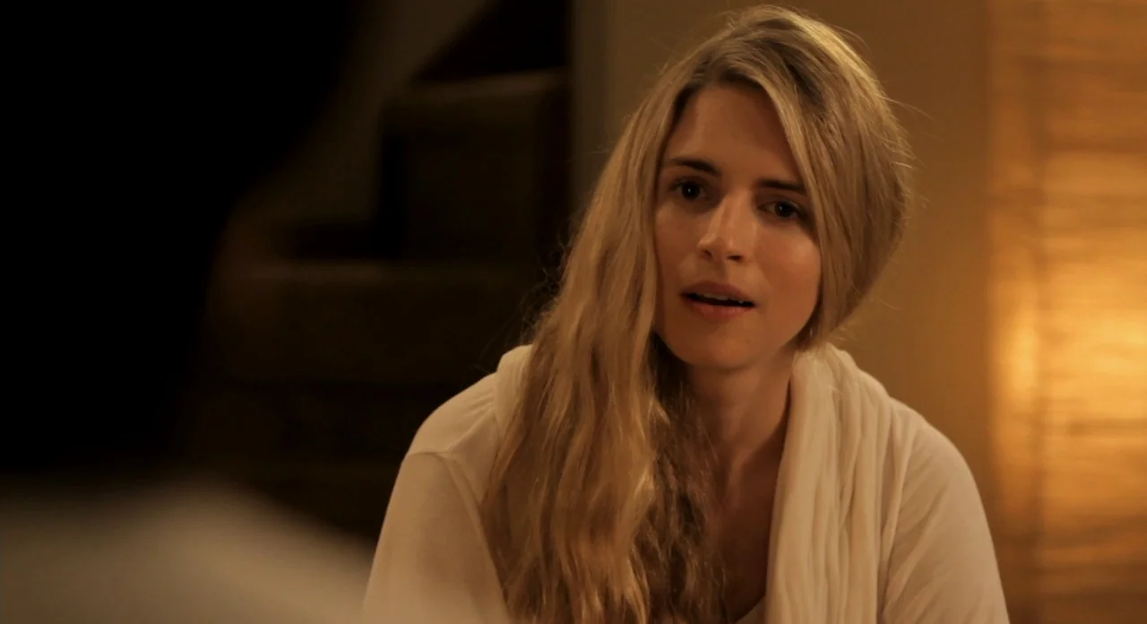 Sound Of My Voice (2011) movie still: medium — A dimly lit room provides a warm, golden-toned backdrop to a woman. A woman with long blonde hair…