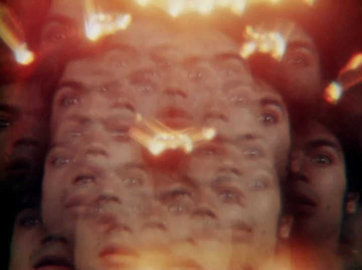 Invocation of My Demon Brother (1969) movie still: closeup — A man's face appears multiple times in a kaleidoscopic refraction effect. Bright light…