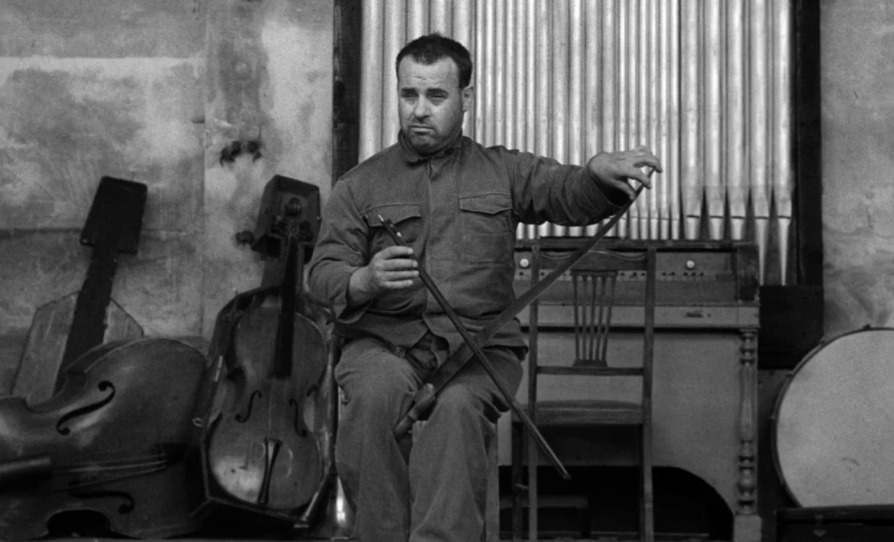 Goto, Island of Love (1969) movie still: medium — A dimly lit room contains musical equipment including an organ and a bass instrument. A man in a…
