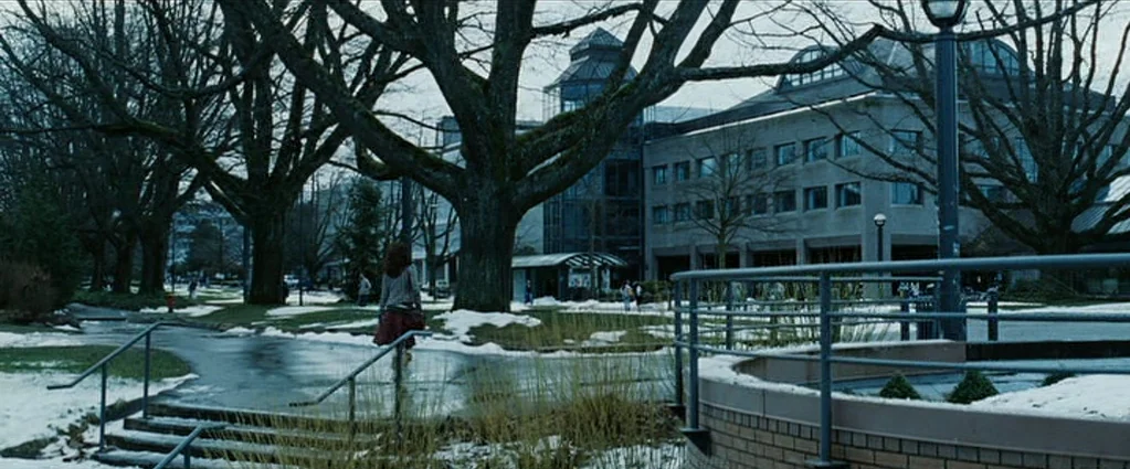 Wind Chill (2007) movie still: wide — A snowy outdoor campus area features a large modern building and leafless trees. A young woman walks away from…