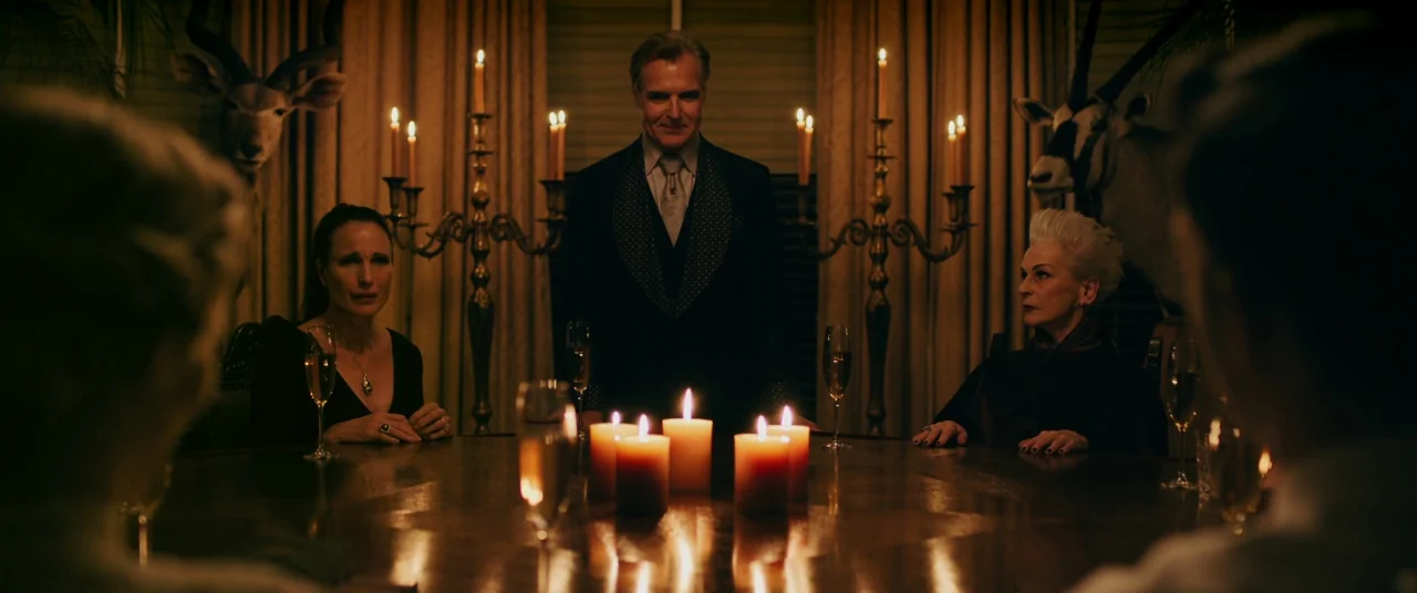 Ready or Not (2019) movie still: medium — A dimly lit room features a formal table set with candles and tall candelabras. A man stands at the head…
