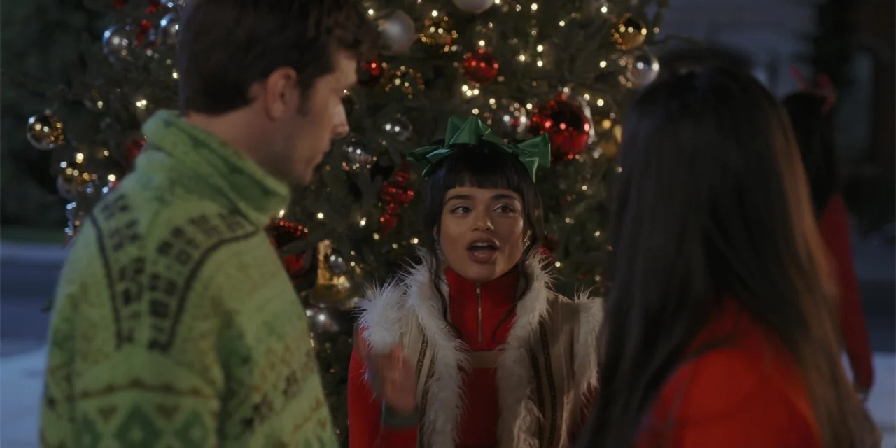 A Hollywood Christmas (2022) movie still: medium — An outdoor area at night features a large, decorated Christmas tree with glowing lights. A woman…