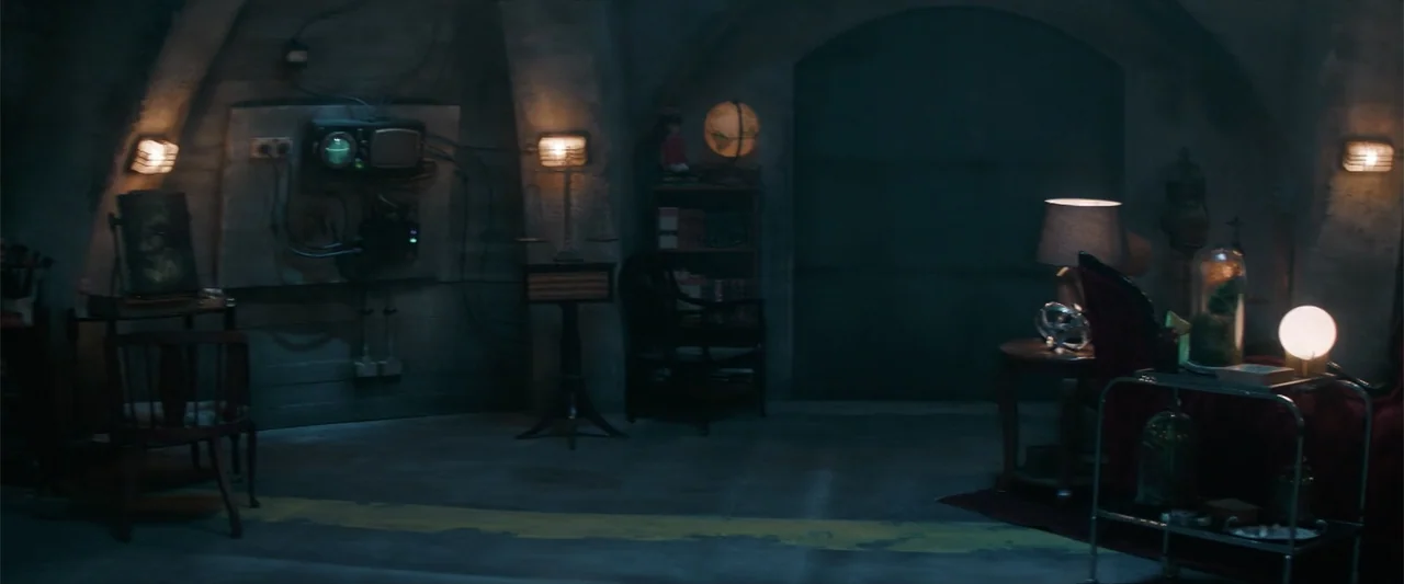M3GAN 2.0 (2025) movie still: wide — A dimly lit concrete bunker interior features arched walls and various vintage furniture pieces. Several lamps…