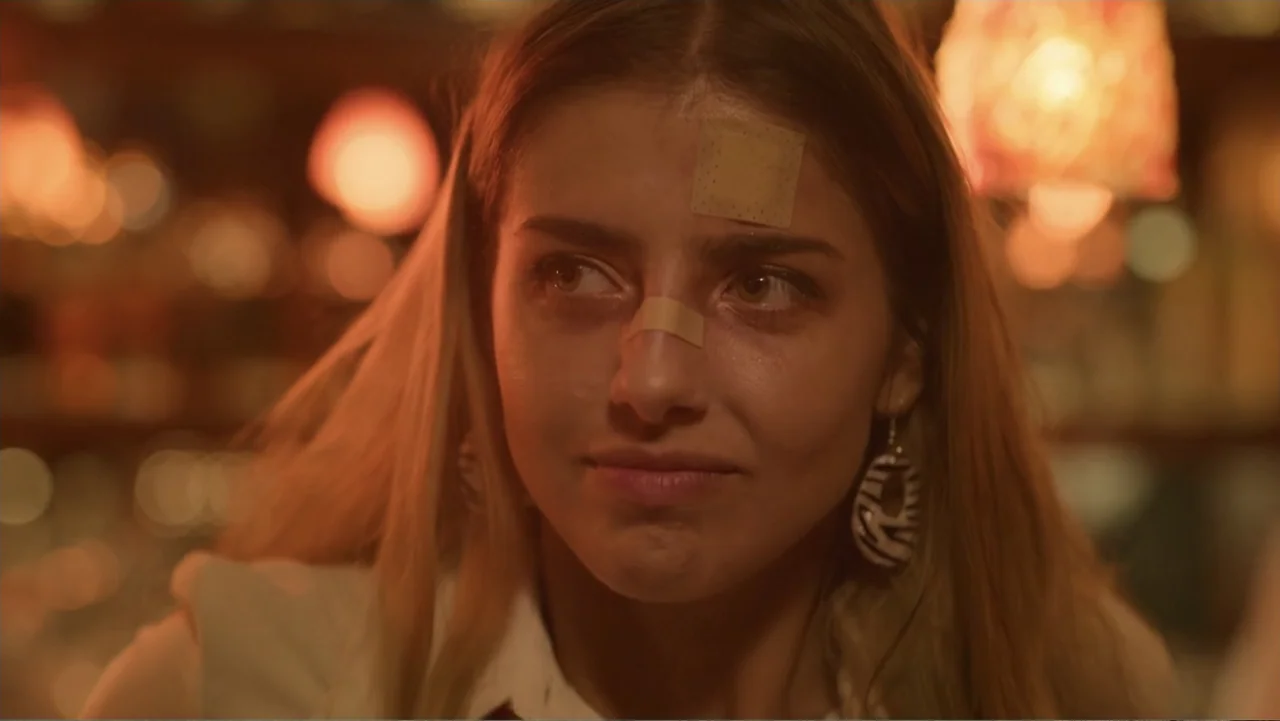 Double Pregnant 2 (2022) movie still: closeup — A dimly lit bar interior features a woman with bandages across her nose and forehead. She sits in…