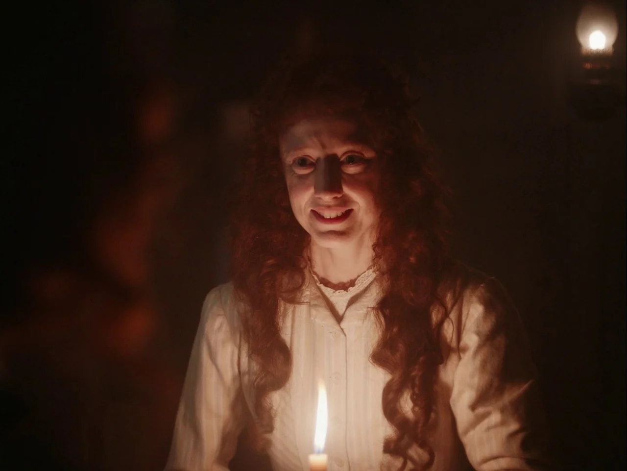 The Electrical Life of Louis Wain (2021) movie still: medium — An interior space lit primarily by the low light of a single candle. A woman with…