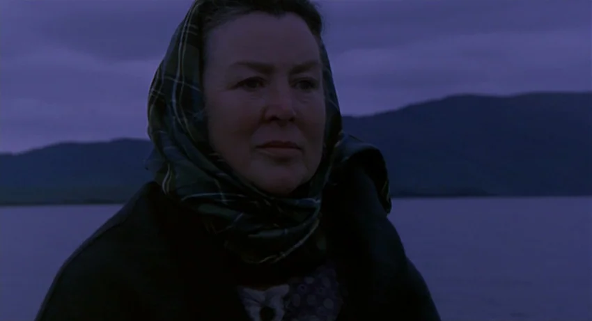 The Secret Of Roan Inish (1994) movie still: medium — An older woman stands before a large body of water under a twilight sky. Dark mountains are…