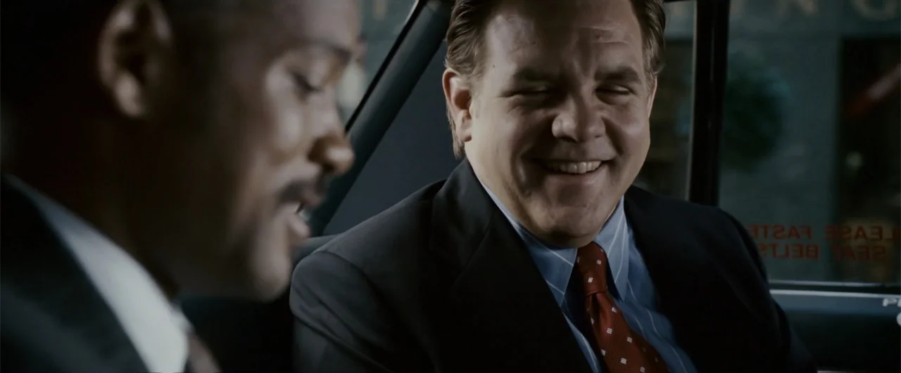 The Pursuit of Happyness (2006) movie still: medium — Two men sit side by side in the backseat of a vehicle. A black man in a suit speaks to a white…