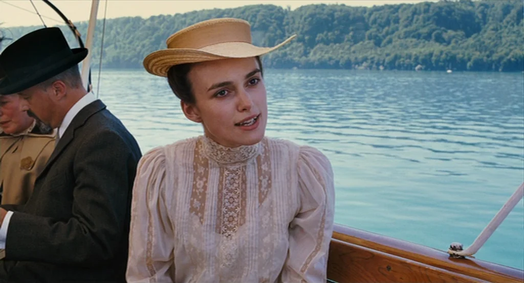 A Dangerous Method movie still: medium — A woman and man sit together on a wooden boat on a sunny day. A vast lake with tree-covered hills in the…