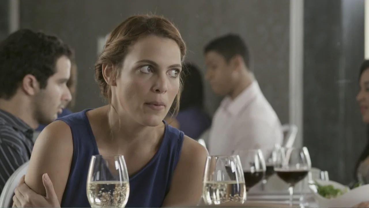 Locas y atrapadas (2014) movie still: medium — A well-lit restaurant interior features patrons seated at tables with wine glasses. A woman in a blue…