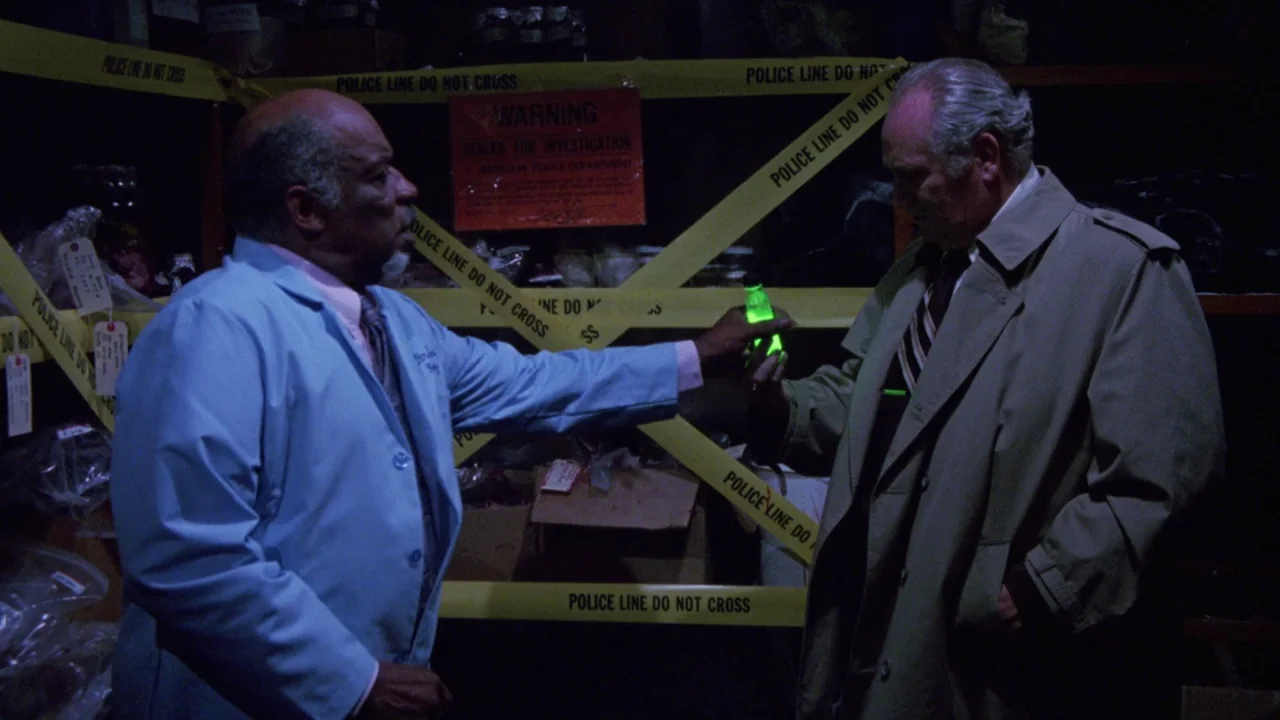 Bride of Reanimator (1989) movie still: medium — A dimly lit room filled with storage shelves covered in yellow police investigation tape. A man in…