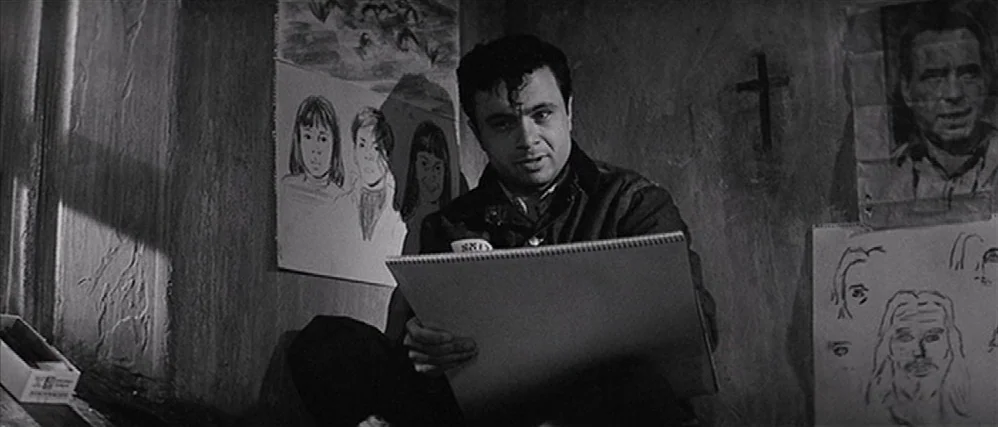 In Cold Blood (1967) movie still: medium — A dimly lit space features textured walls covered in various pencil and ink drawings. A young man sits…
