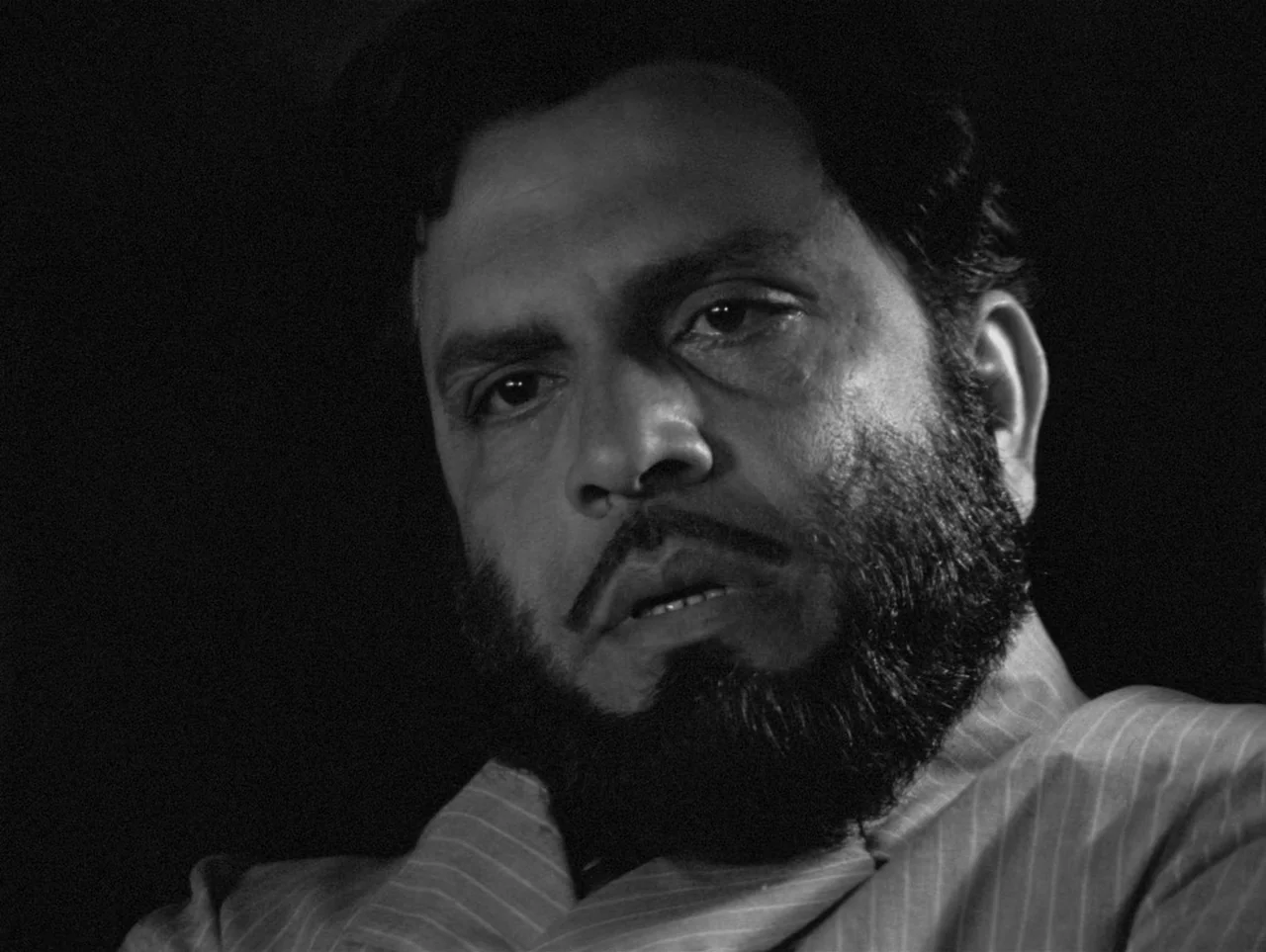 Charulata (1964) movie still: closeup — An undifferentiated dark space frames the upper torso and head of a man. The subject gazes towards the left…