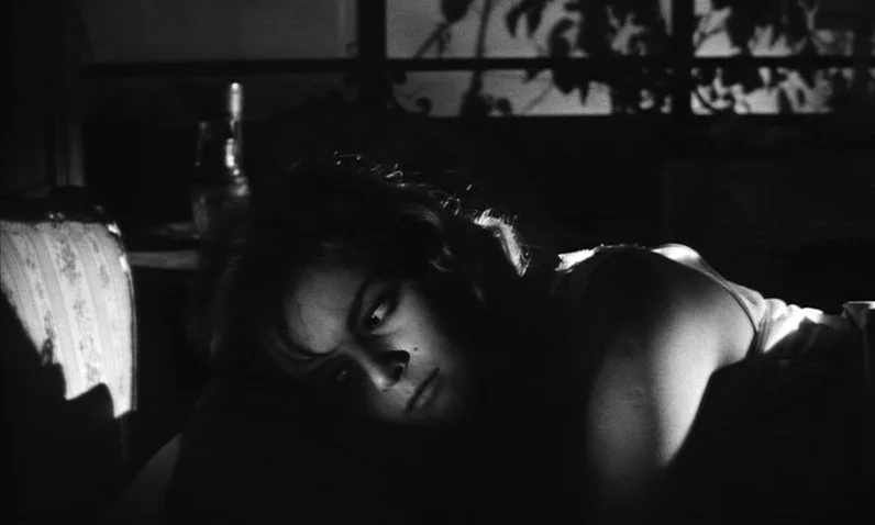 The Girl Who Knew Too Much (1963) movie still: closeup — A dark bedroom features a woman resting her head on a pillow. Light streams through a…