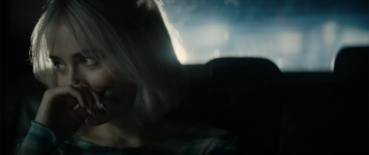Daddio (2024) movie still: closeup — A dark vehicle interior with the subject visible in the back seat at night. The woman rests her hand near her…