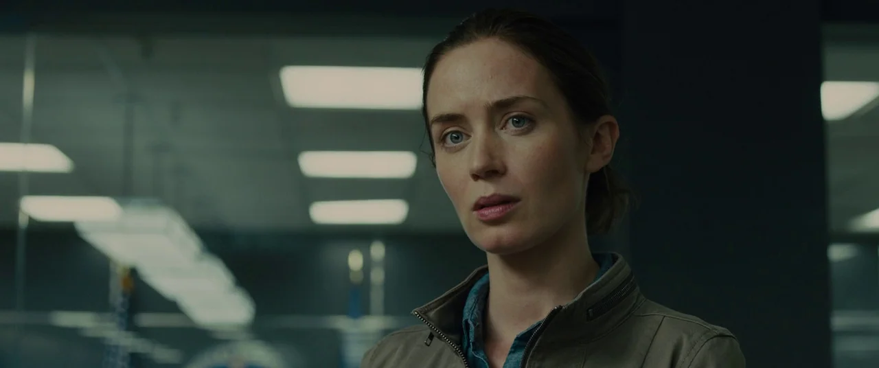 Sicario (2015) movie still: closeup — A modern, professional interior space featuring drop ceilings with recessed fluorescent panel lights. A woman…