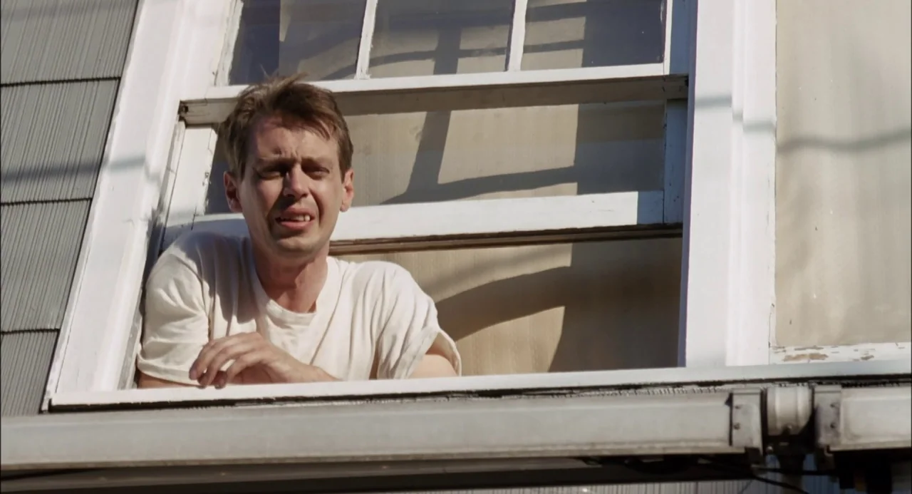 Trees Lounge (1996) movie still: medium — A man looks out from a window of a residential building during the day. The building has light-colored…