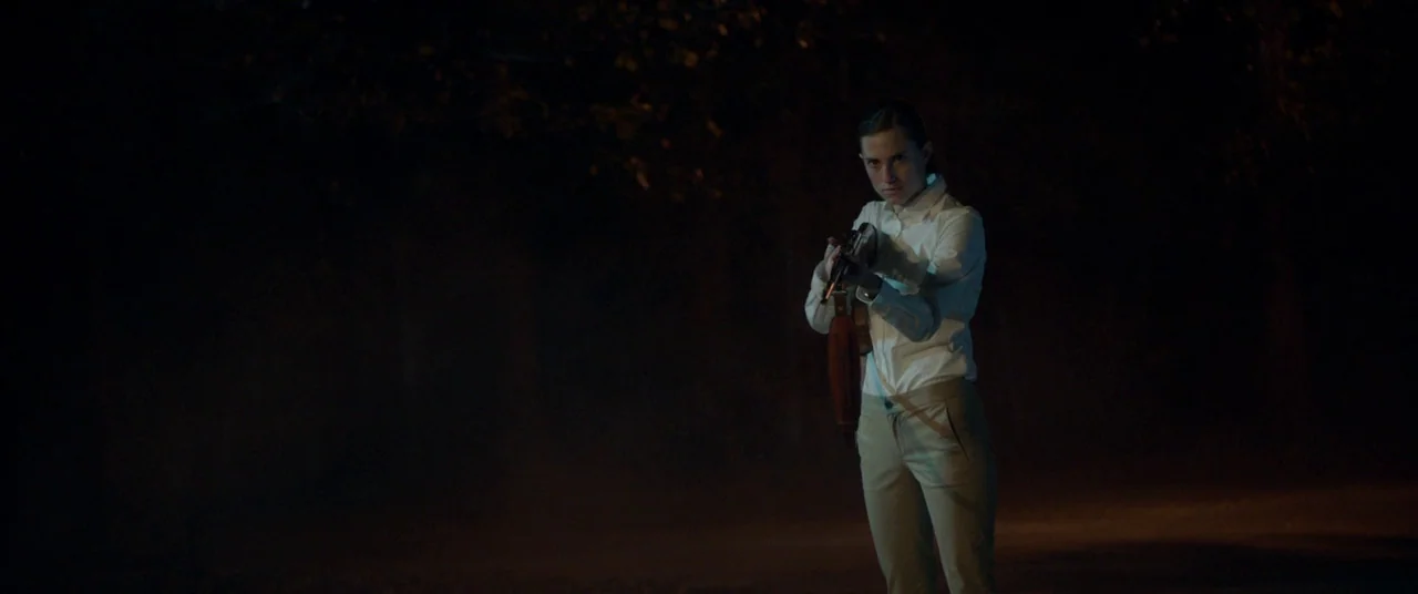 Get Out (2017) movie still: medium — A dark, unlit road at night with barely visible surrounding foliage. A woman stands in the middle of the road,…