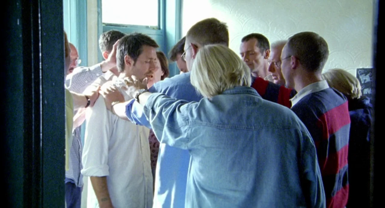 My Summer of Love movie still: medium — A group of diverse individuals stands in a circle inside a brightly lit room. They gather around a central…