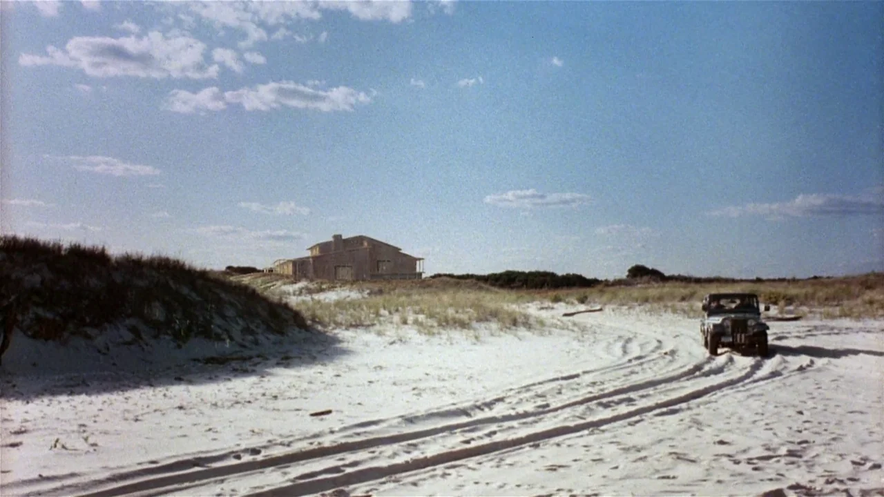 Creepshow (1982) movie still: wide — A wide sandy landscape features dunes topped with sparse grass under a clear sky. A jeep travels along a set of…
